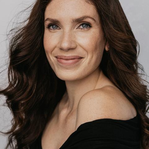 Woman with long flowing hair smiling directly at the camera wearing an off the shoulder sweater