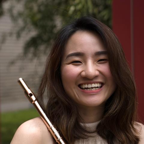 Woman in halter dress holds a flute across her right shoulder smling directly at the camera