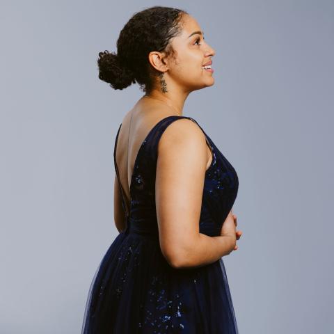 Woman with hair pulled back and wearing a formal dress looking off camera to the right and smiling