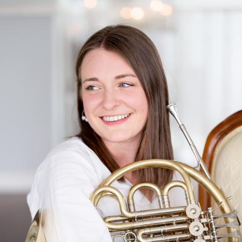 Woman holding a french horon looking off camera and smiling