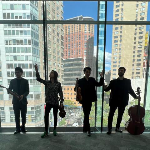 Members of Napoletano Quartet backlit in front of a large window showing a city scape behind them
