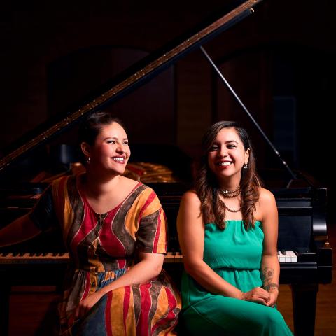 members of Obsidiana Duo sitting on piano bench in front of piano