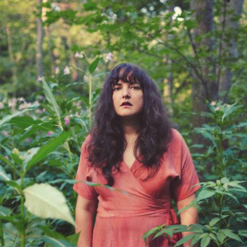 Abigail stands outdoors in a pink dress, looking at the camera.