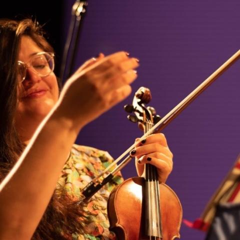 Alejandra pictured here with a purple background holding a violin. 