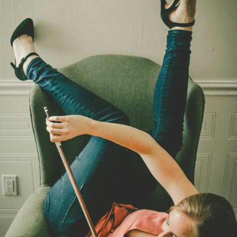 Lauren lays on a chair and plays a violin. She is wearing jeans and smiles.