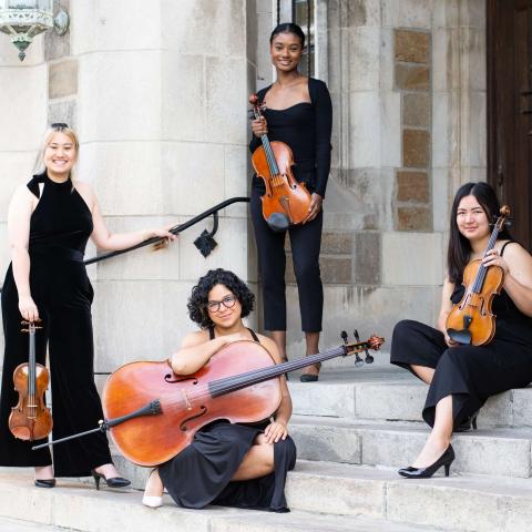 The Calista Quartet member sit on stairs out front of a building. They wear black and hold their instruments. 