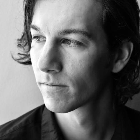 Black and white close up photo of Alex Ellsworth. He has long wavy hair pushed to the left. 