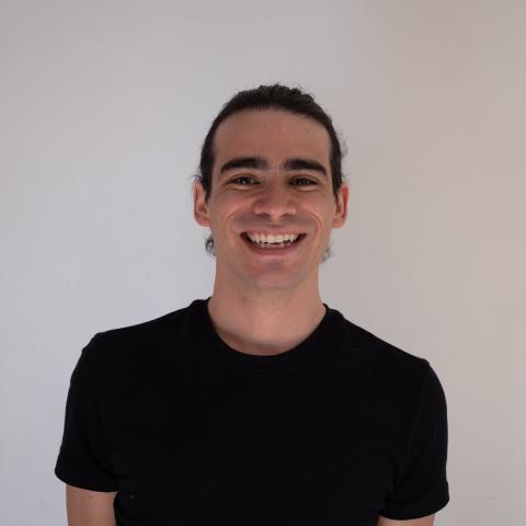 Sebastián stands in front of a white wall, smiling. He is wearing a black t-shirt. 