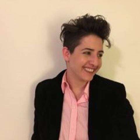 Fay Nass stands against a beige background and looks off to the side, smiling.