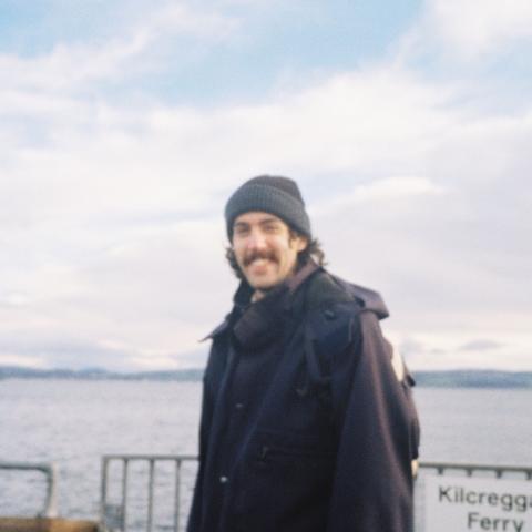 A blurry photo of Ollie sanding outdoors in front of clouds wearing a toque. 