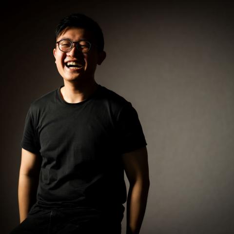 Bevis wears a black shirt and is smiling in front of a grey backdrop.