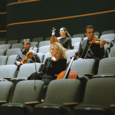 The members of the Vaughan String Quartet sit in the audience seats of a theatre holding their instruments