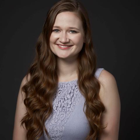 Woman with long flowing wavy hair smiling directly at the camera and wearing a light puple formal dress