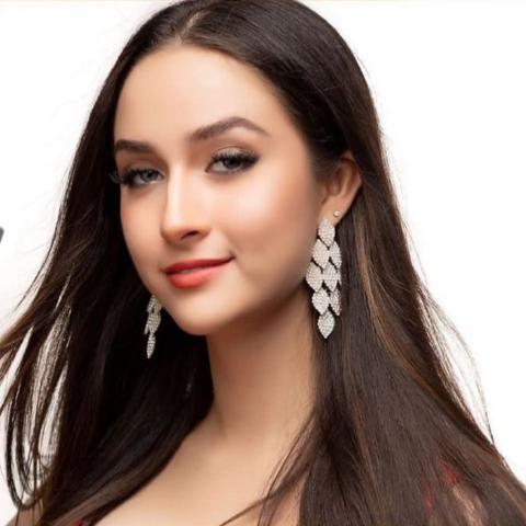 Close up shot of a woman wearing large dangly earings and smiling slightly at the camera