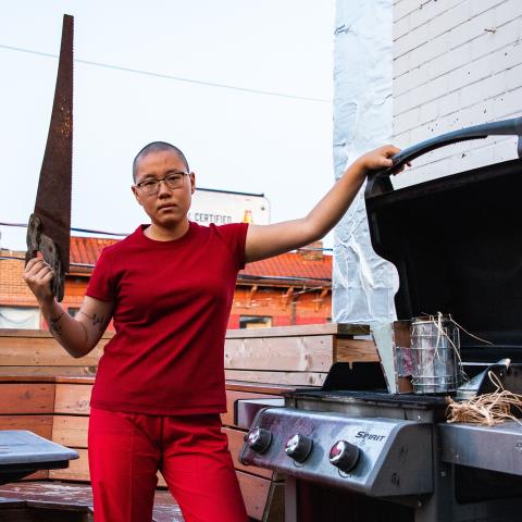A person standing at an open barbecue dressed all in red and holding a saw