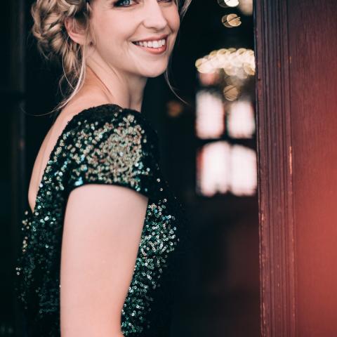 Blond smiling person standing in doorway looking back at camera in sparkly dress