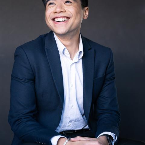 Smiling person looking off camera, hands clasped in lap