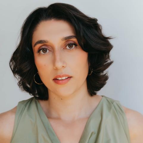 Woman standing with hands behind her back on hips looking directly at the camera