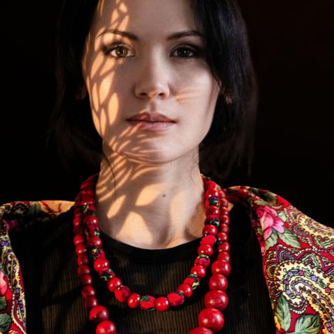 Person looking into the camera wearing a red necklace and colour top