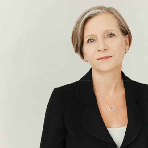 Woman with short blonde hair and black jacket smiling softly at the camera