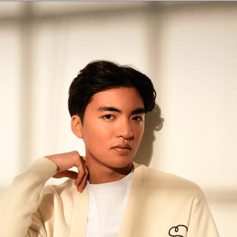 Man in the shadow of a window looking at the camera in a casual white artsy sweater