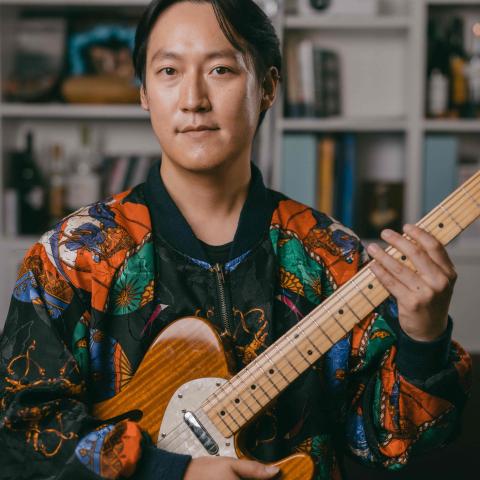 Man holding string instruments with colourful jacket on looking at the camera