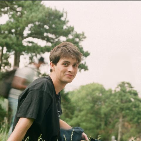 Casually dressed man sitting outside amongst trees looking at camera
