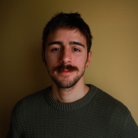 Man standing against wall in dark room smiling at camera