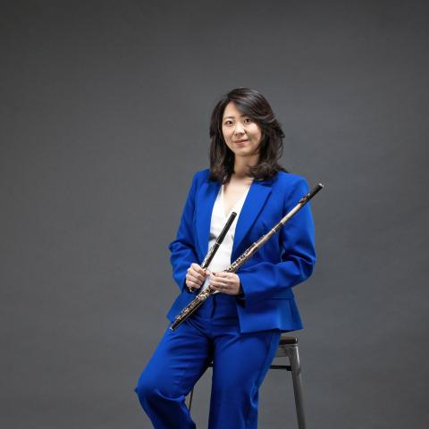 Woman in royal blue suit leaning against a stool holding instrument