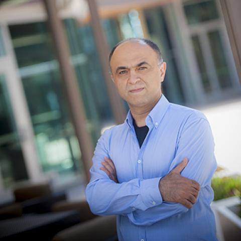 Man wearing blue button down standing outside with arms crossed in front of chest